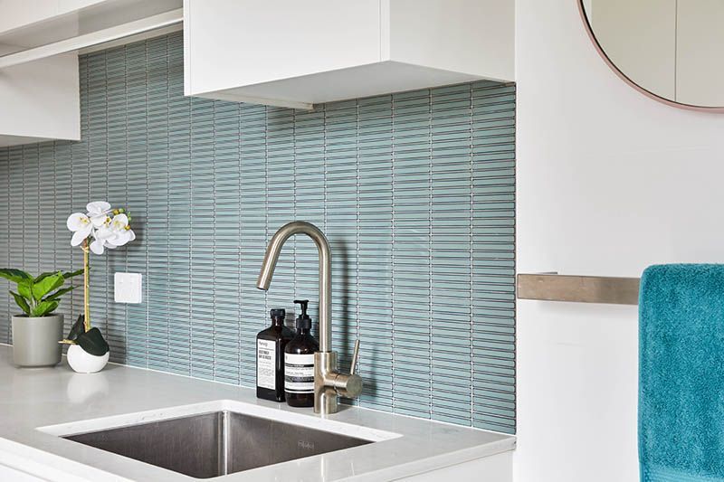 A kitchen with a sink , faucet , mirror and towel rack.