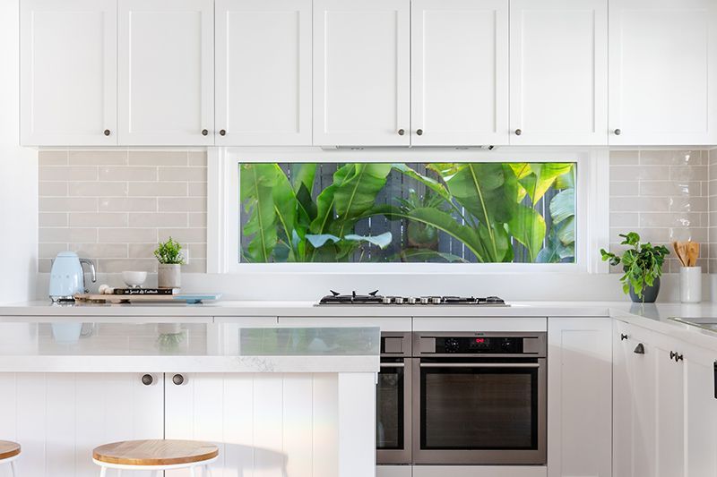 A kitchen with white cabinets , stainless steel appliances , a stove and a window.