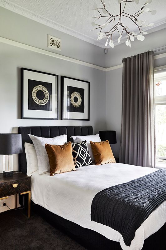 A bedroom with a bed , two lamps , two pictures on the wall and a chandelier.
