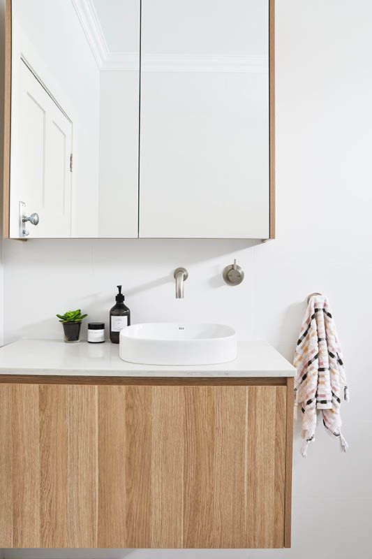 A bathroom with a sink , mirror and wooden cabinets.