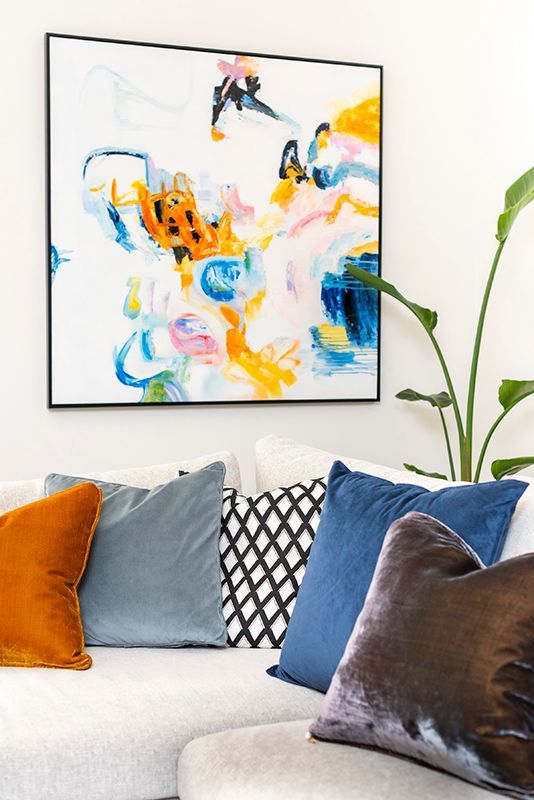 A living room with a couch , pillows and a painting on the wall.