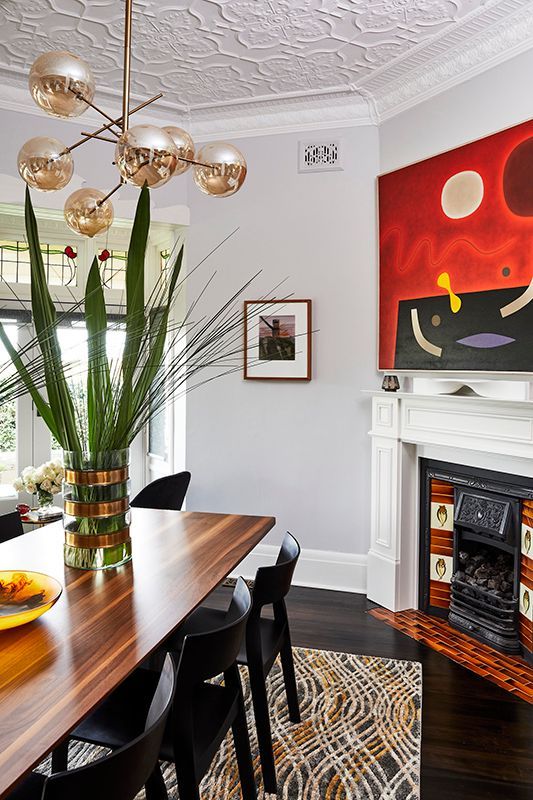 A dining room with a table , chairs , a fireplace and a painting on the wall.