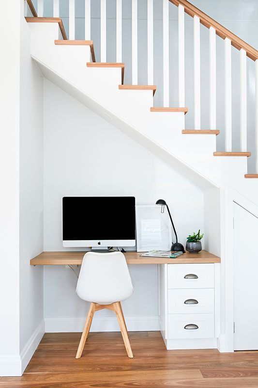 There is a desk under the stairs with a computer on it.