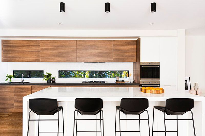 A kitchen with wooden cabinets , white counter tops , and black stools.