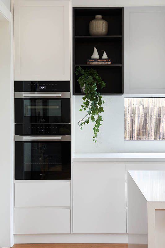 A kitchen with white cabinets and black appliances and a plant hanging from the wall.