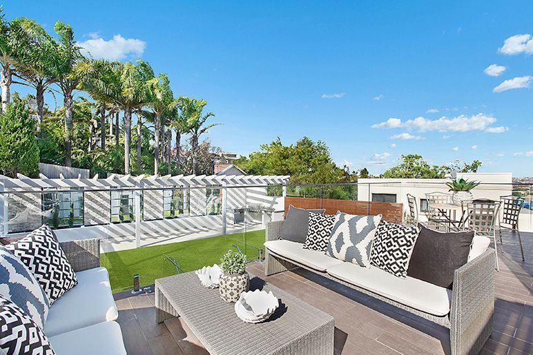 A patio with a couch , table , and palm trees in the background.