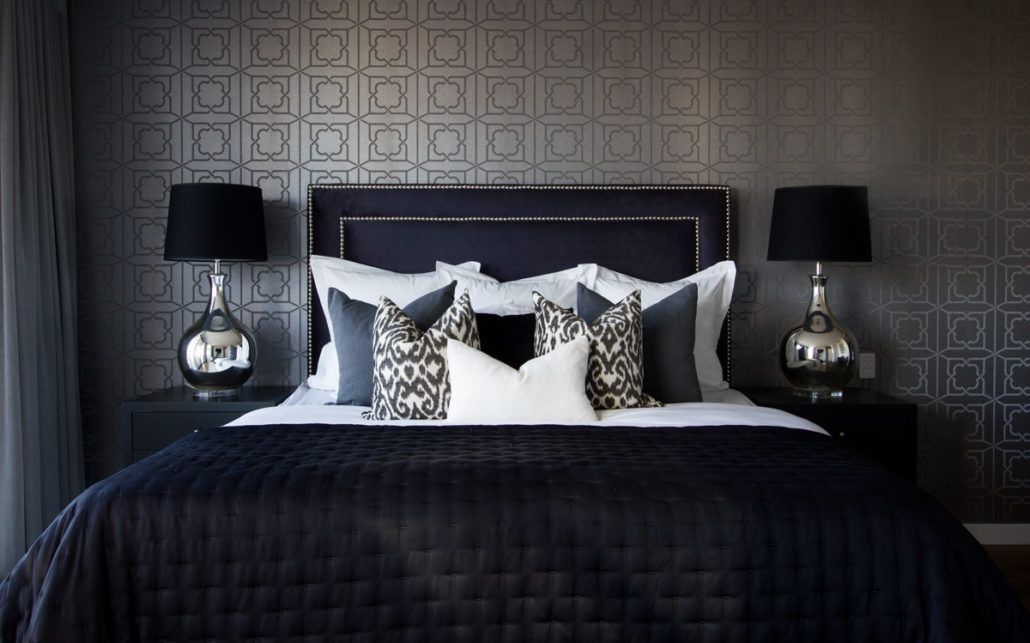 A bedroom with a bed , two lamps , and a black headboard.