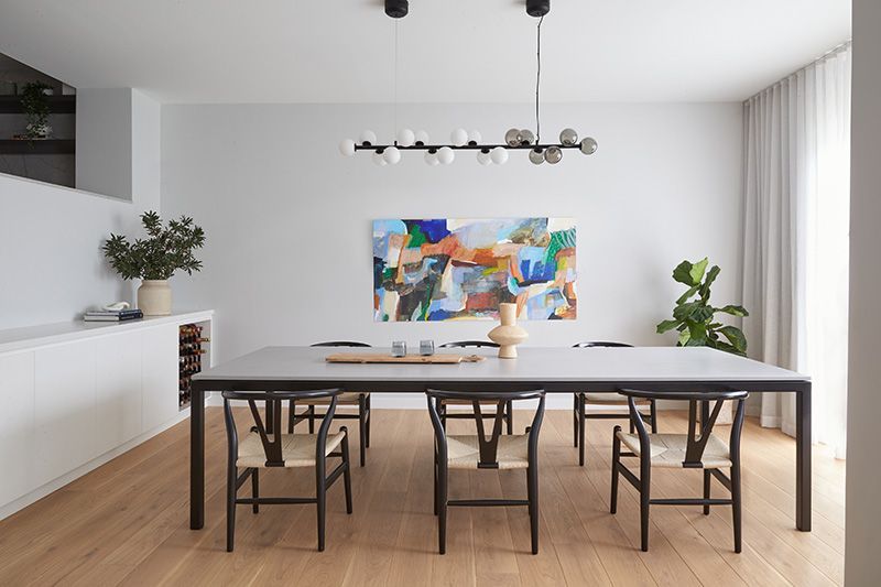 A dining room with a long table and chairs and a painting on the wall.