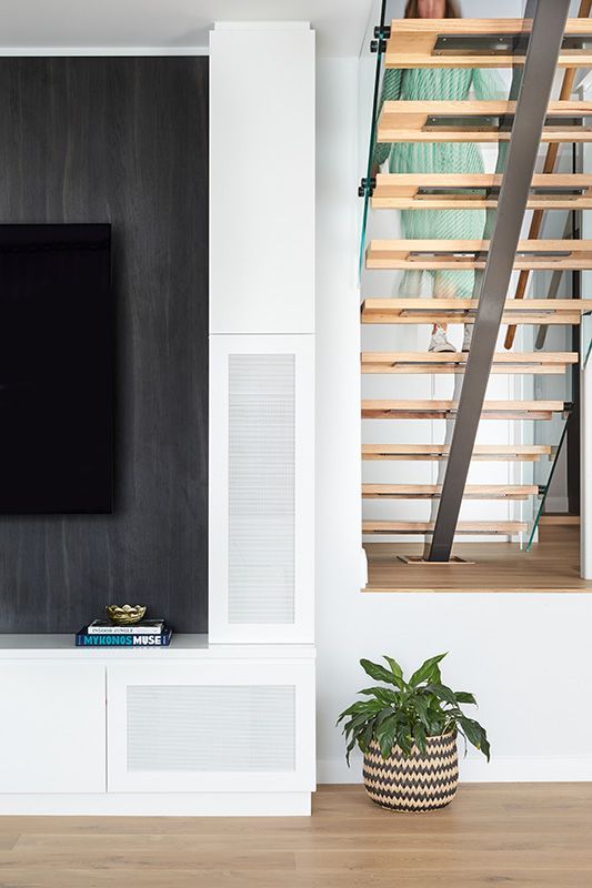 A living room with a tv , stairs and a potted plant.