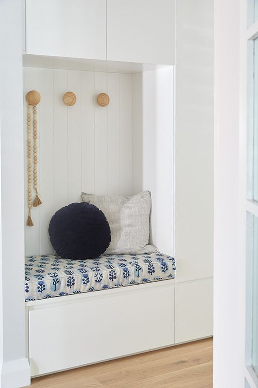 A white bench with a blue and white cushion and pillows in a hallway.