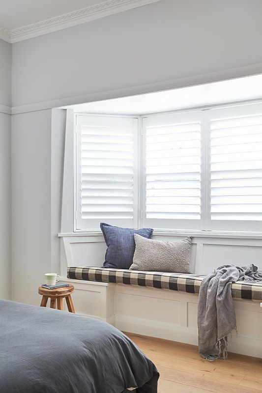 A bedroom with a bed and a window seat with shutters.