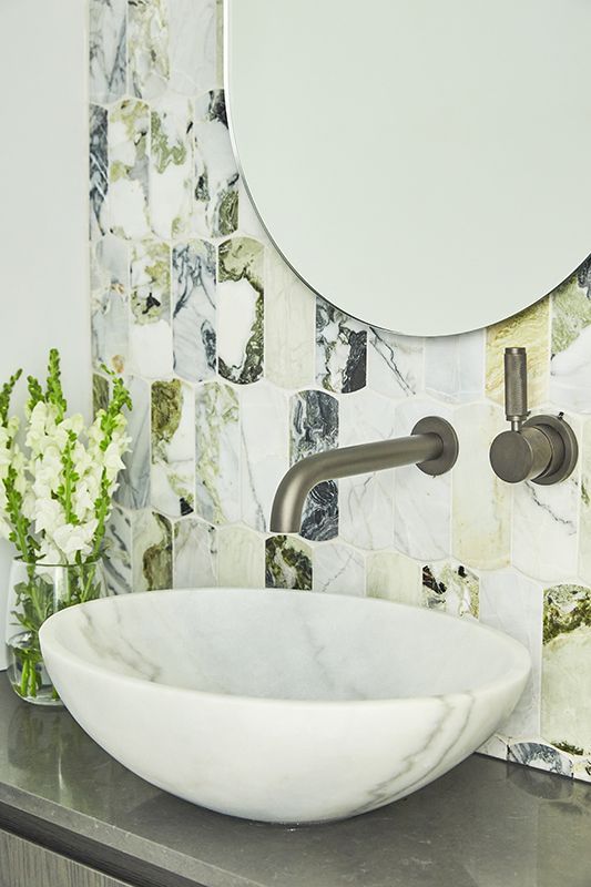 A bathroom with a sink , mirror , and vase of flowers.