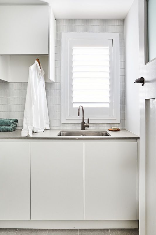 A laundry room with white cabinets , a sink , and a window.