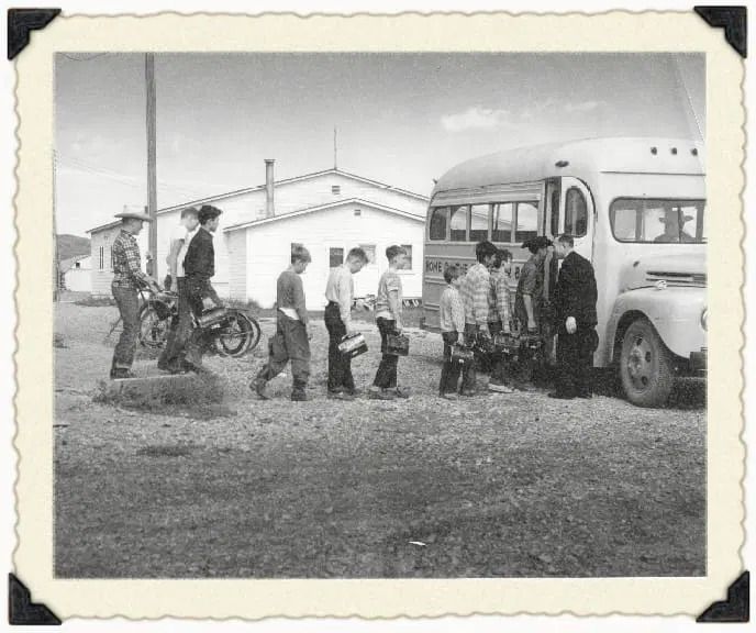 A group of people board a bus parked in front of a building on a gravel lot.