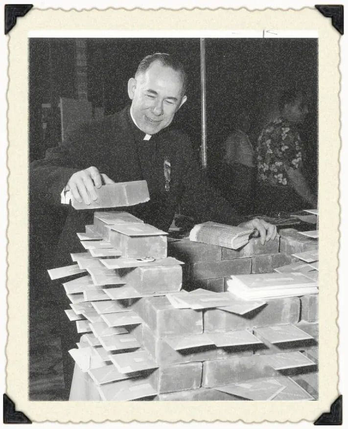 A priest smiling while laying bricks for a wall construction project.