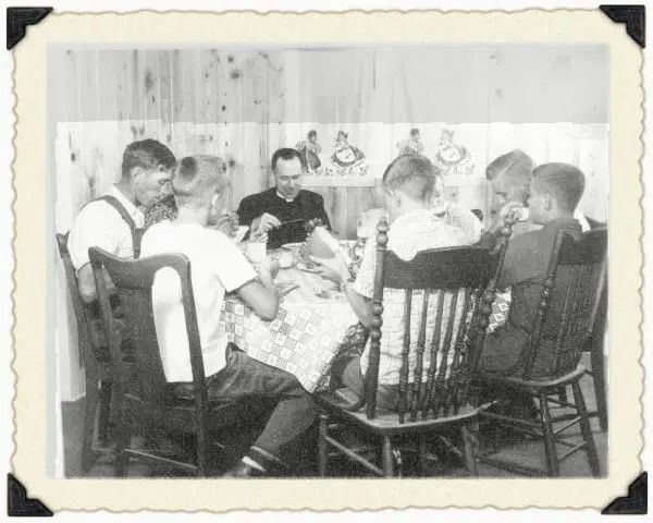 A group of people sitting around a dining table in a bright room, looking down at items on the table.