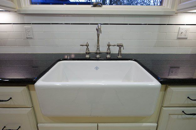Kitchen sink beneath a window, with white apron-front basin and dark countertops.