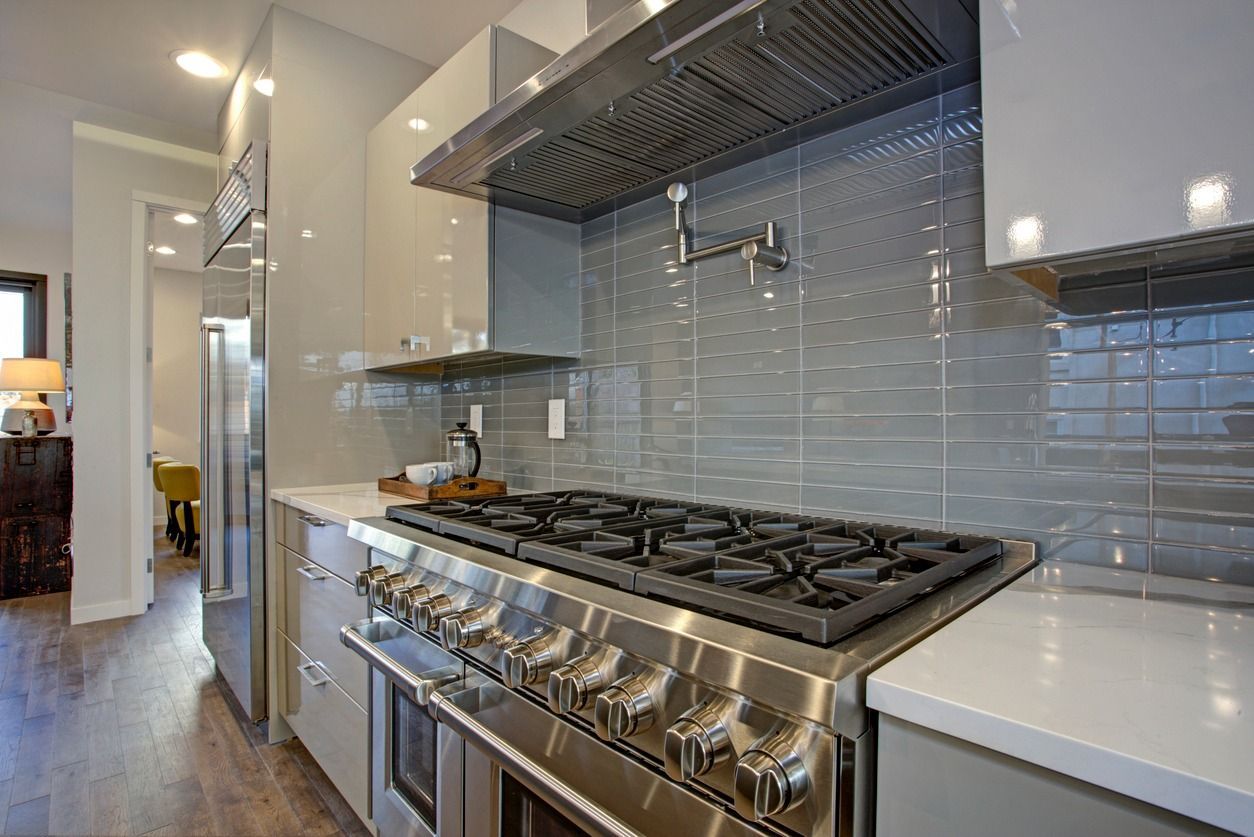 Modern kitchen with stainless steel gas range, gray tile backsplash, and white countertops
