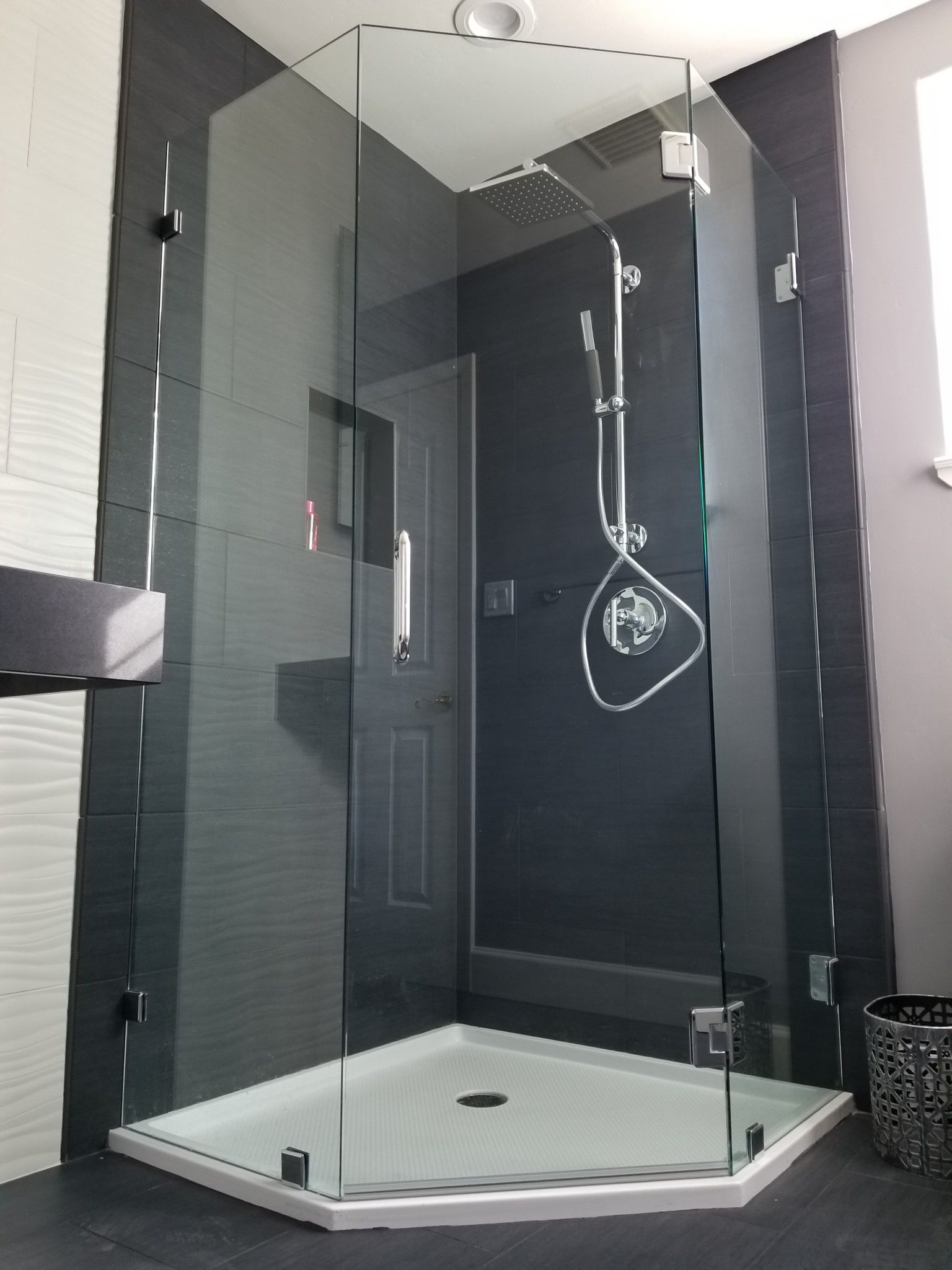 Glass walk-in shower with white tile base and dark tiled walls in a modern bathroom