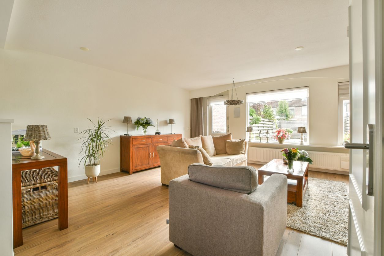 Bright living room with beige sofa, armchair, wooden cabinet, and large window with natural light