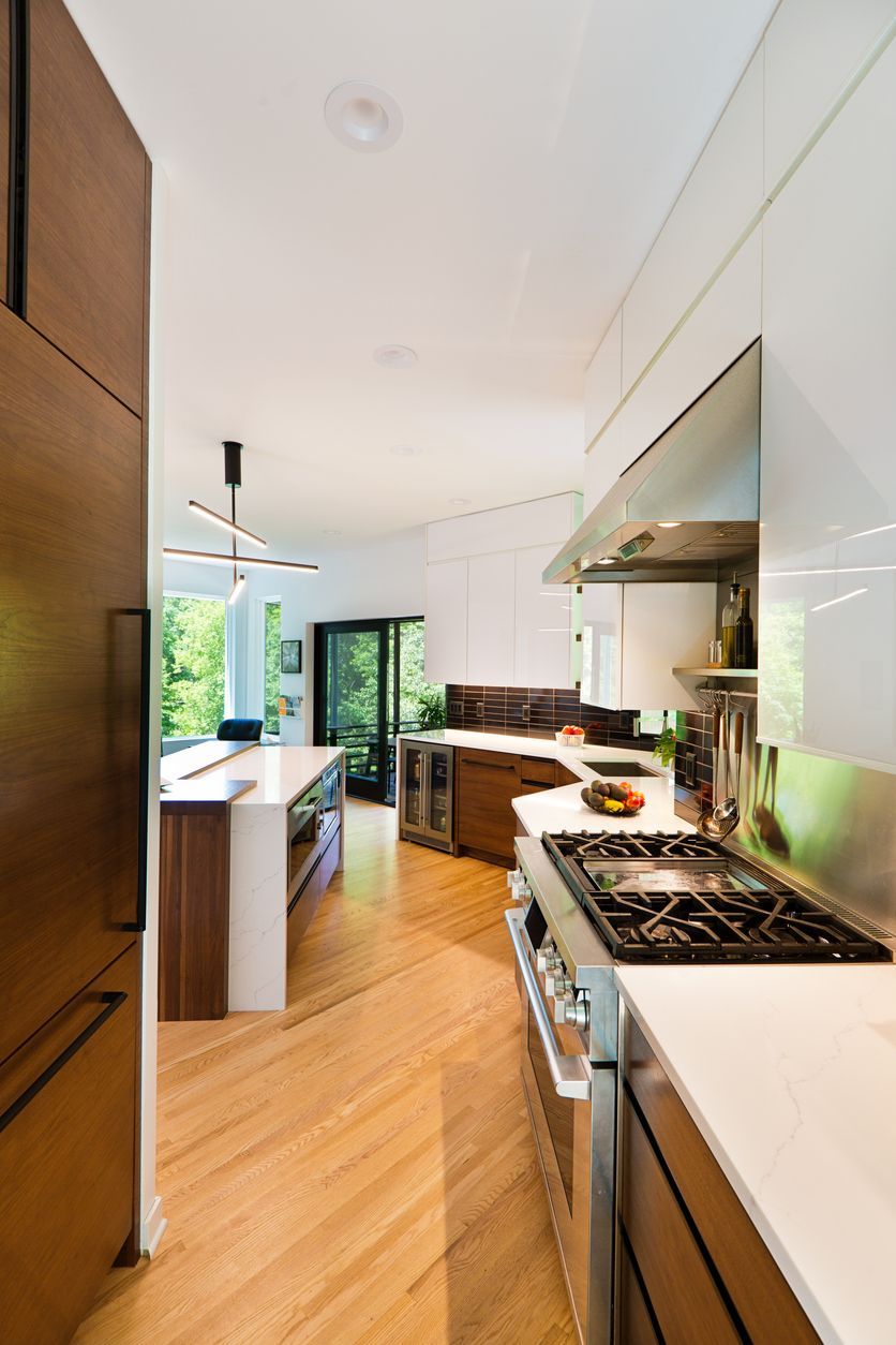 Modern kitchen with wood floors, white cabinets, stainless stove, and island near a bright window.