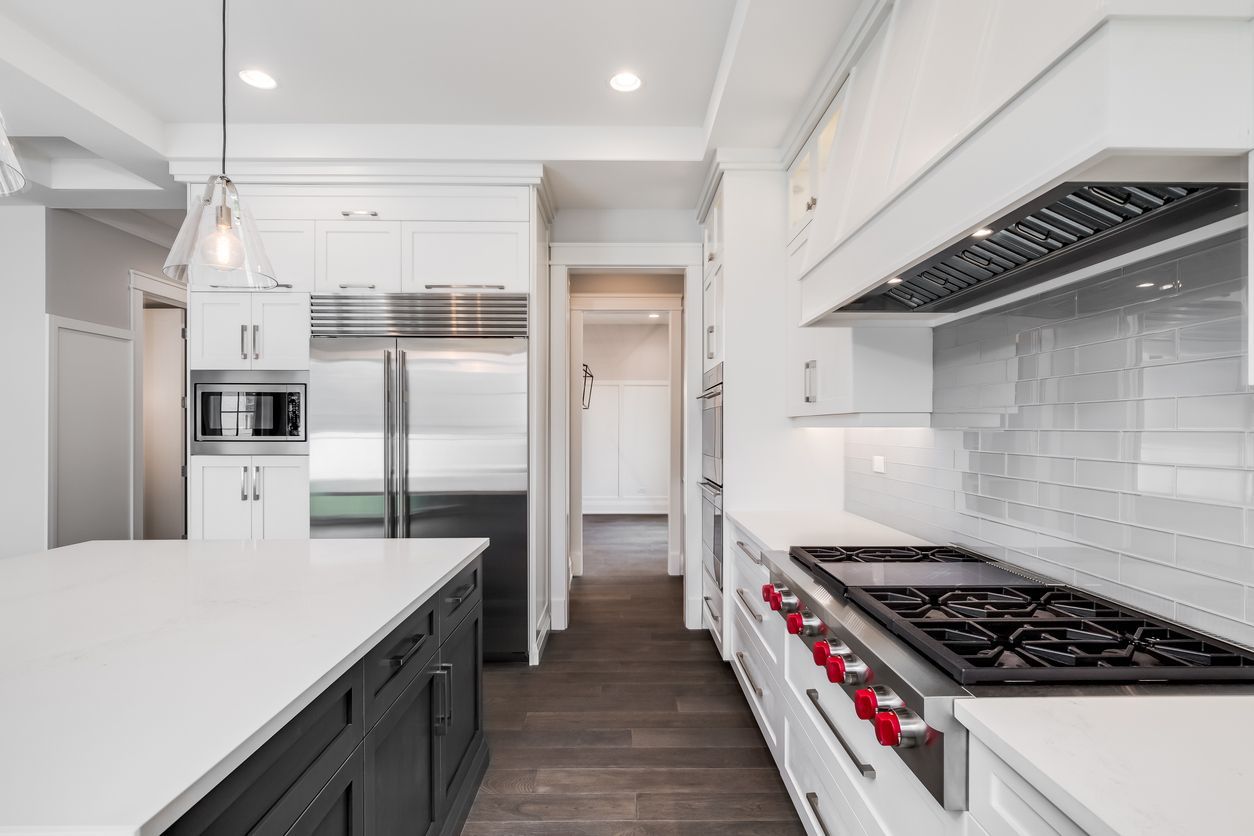 Modern white kitchen with island, stainless steel appliances, dark wood floor, and gas range
