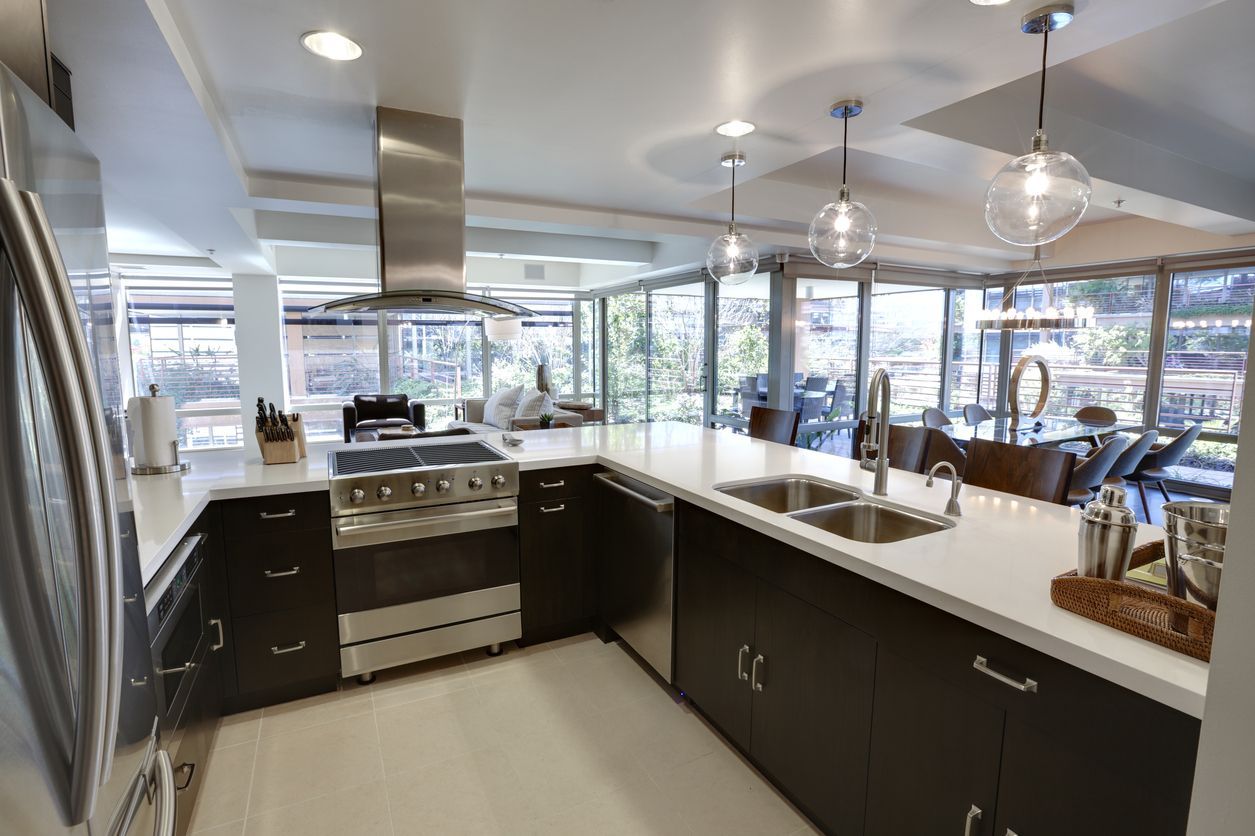 Modern kitchen with dark cabinets, stainless appliances, island sink, and large windows overlooking a patio
