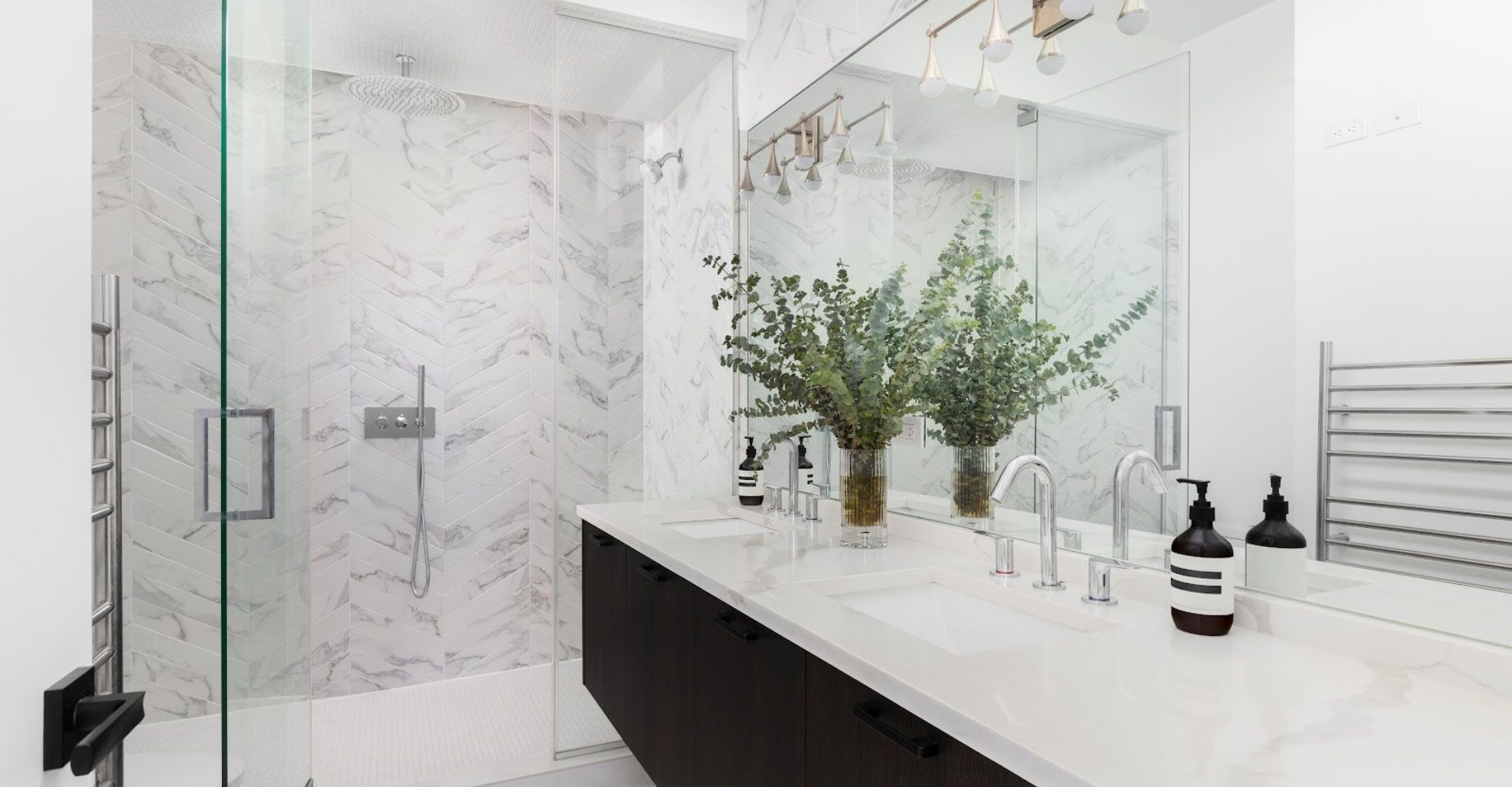 Modern white bathroom with marble shower, black vanity, mirror, and greenery on the counter
