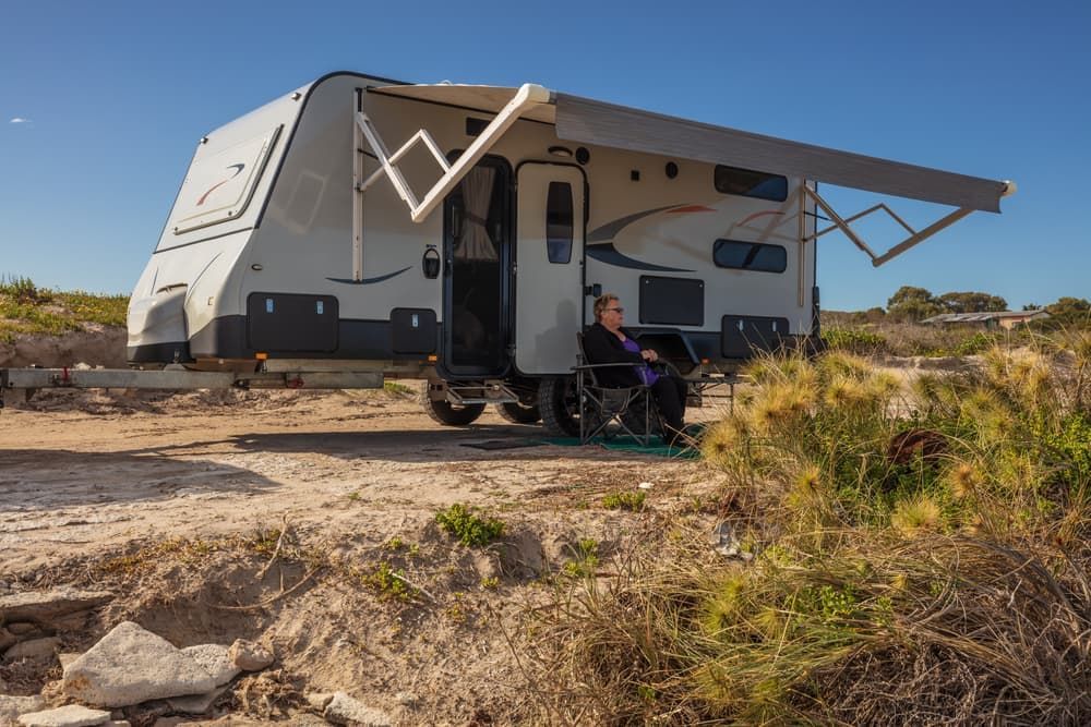 A Person Sits Outside a Grey Caravan with Awning Extended — Darwin Caravan & RV Centre In Berrimah, NT