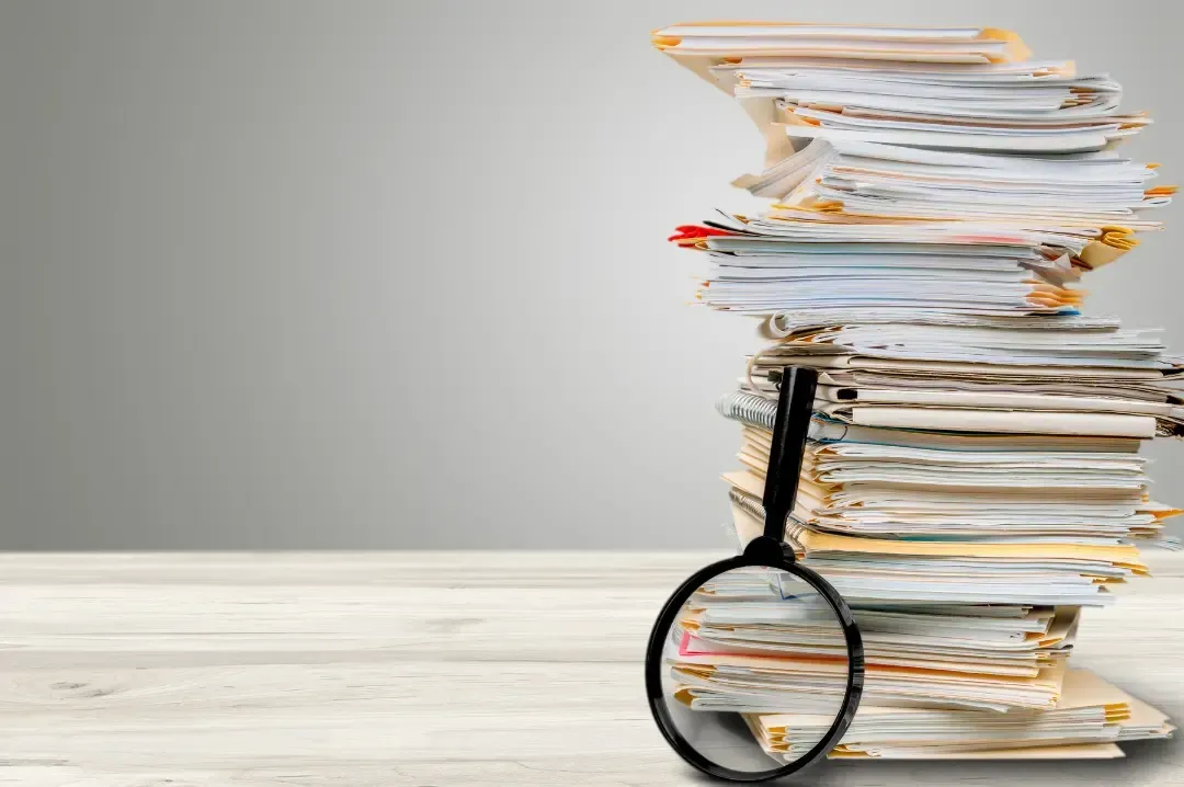A magnifying glass is sitting next to a stack of papers.