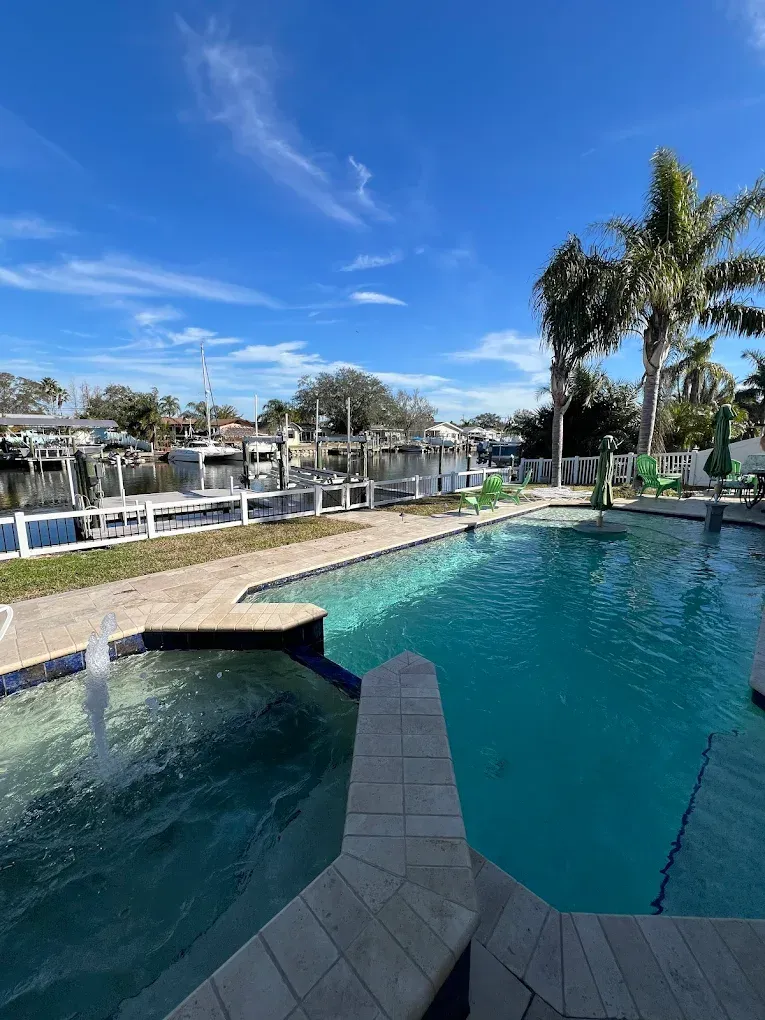 Resort pool with a water slide, palm trees, and a clear blue sky by waterfront cottages