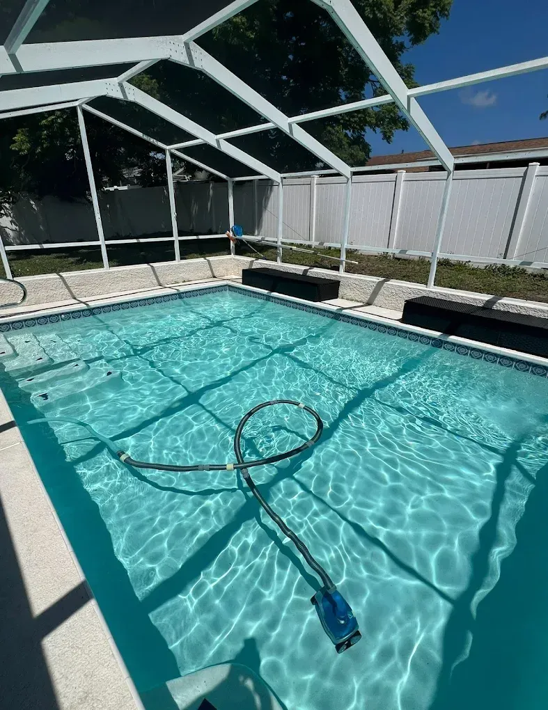 Screened backyard pool with a pool vacuum floating in clear blue water