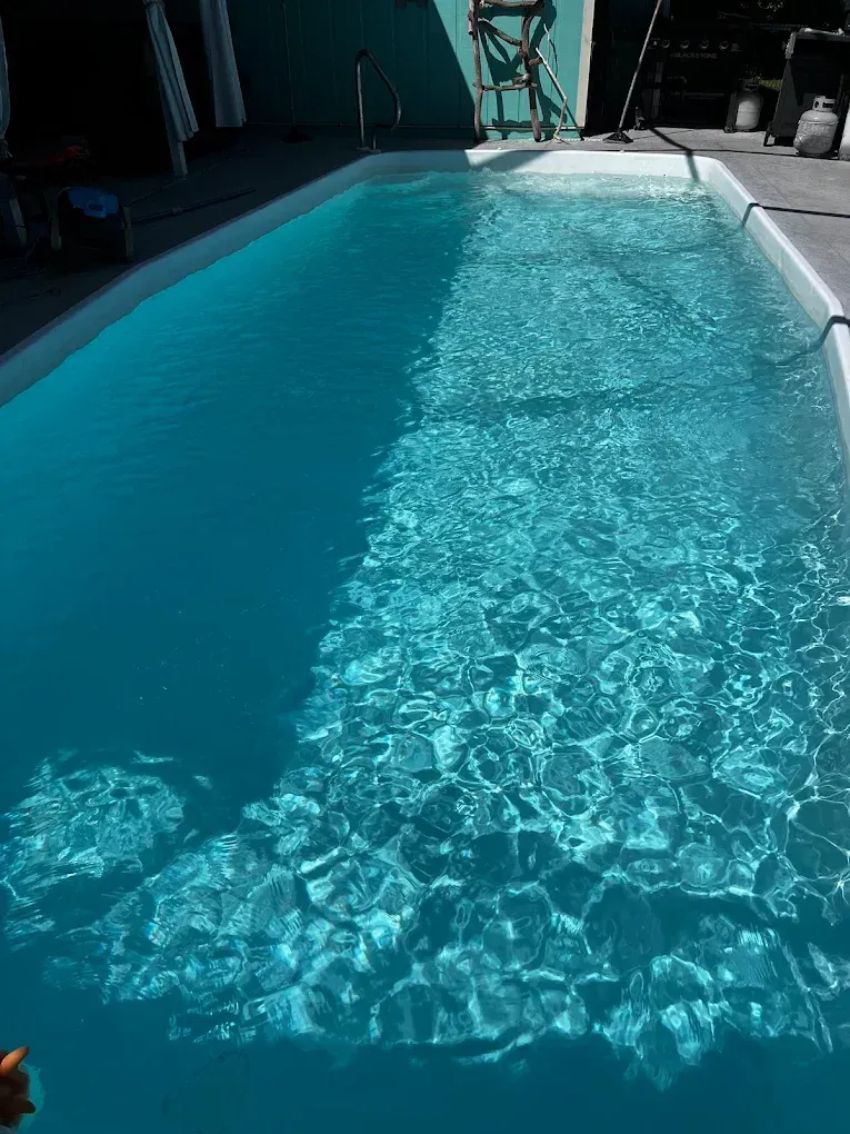 Sunny blue swimming pool with rippling water beside a tiled deck
