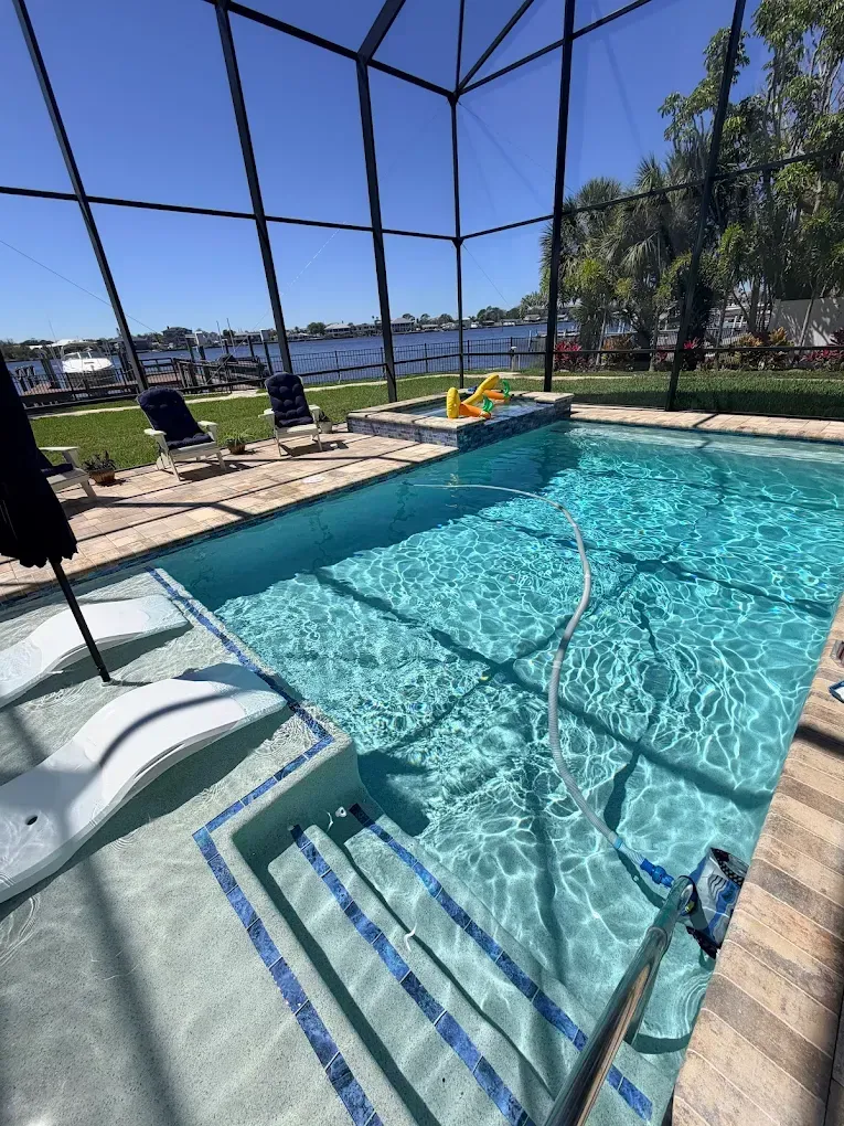 Screened backyard pool with lounge chairs, dock, and water view on a sunny day