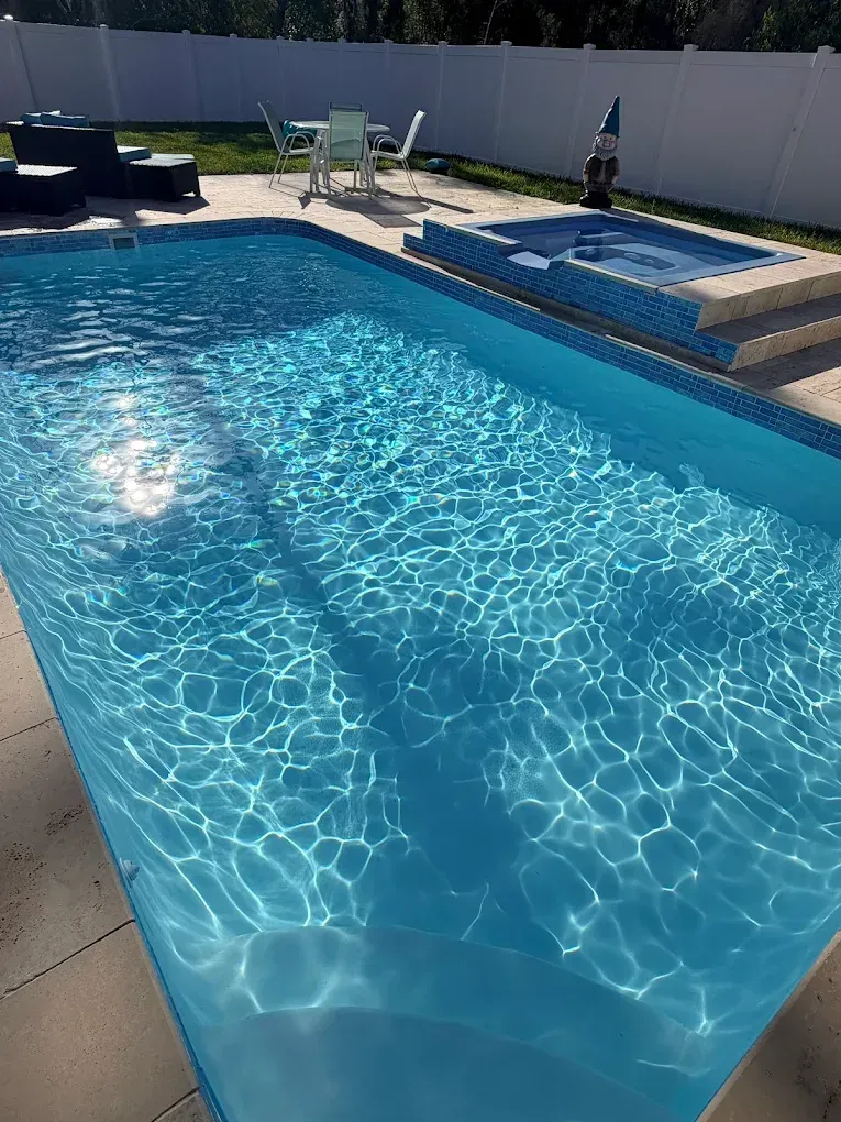 Sunny backyard swimming pool with blue water, lounge chairs, and a white fence.