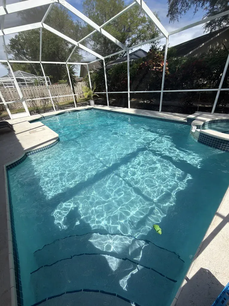 Screened-in backyard swimming pool with clear blue water and lounge chairs around it