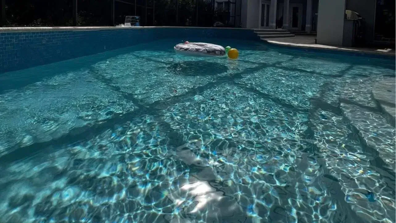 Screened backyard pool with a pool vacuum floating in clear blue water