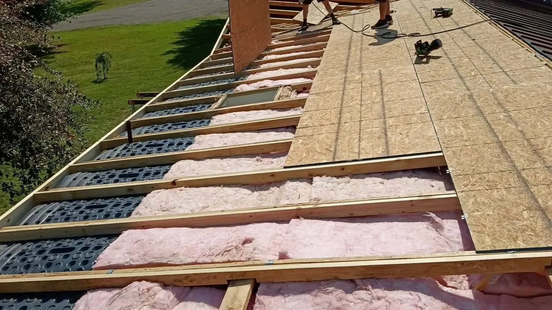 Attic ventilation baffles and fiberglass insulation installed beneath new roof decking in Grant, MI