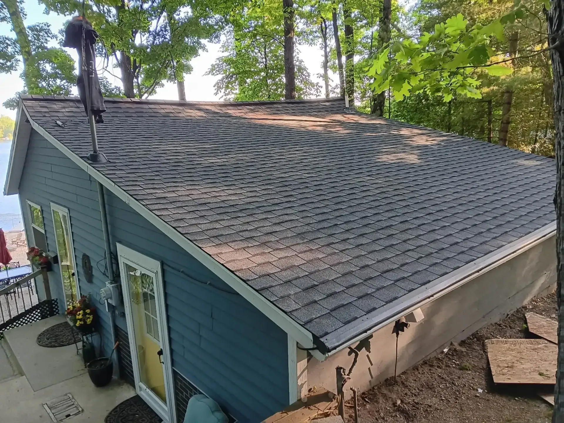 Blue house with a steep shingled roof, viewed from above beside trees and water