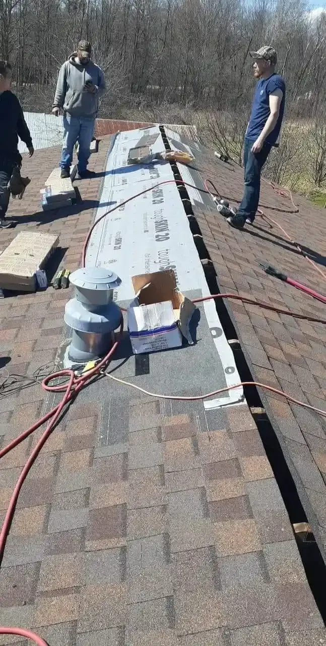 Our team working on a shingled roof, with tools and materials laid out along the ridge.