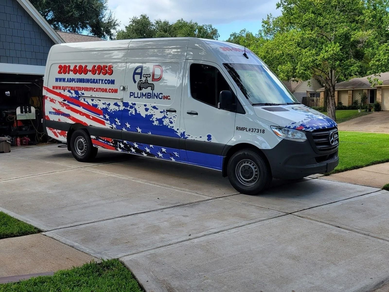 White plumbing service van with red and blue graphics parked in a suburban driveway