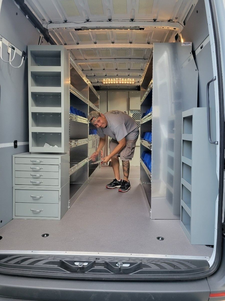 Person installing shelving inside a white cargo van interior.
