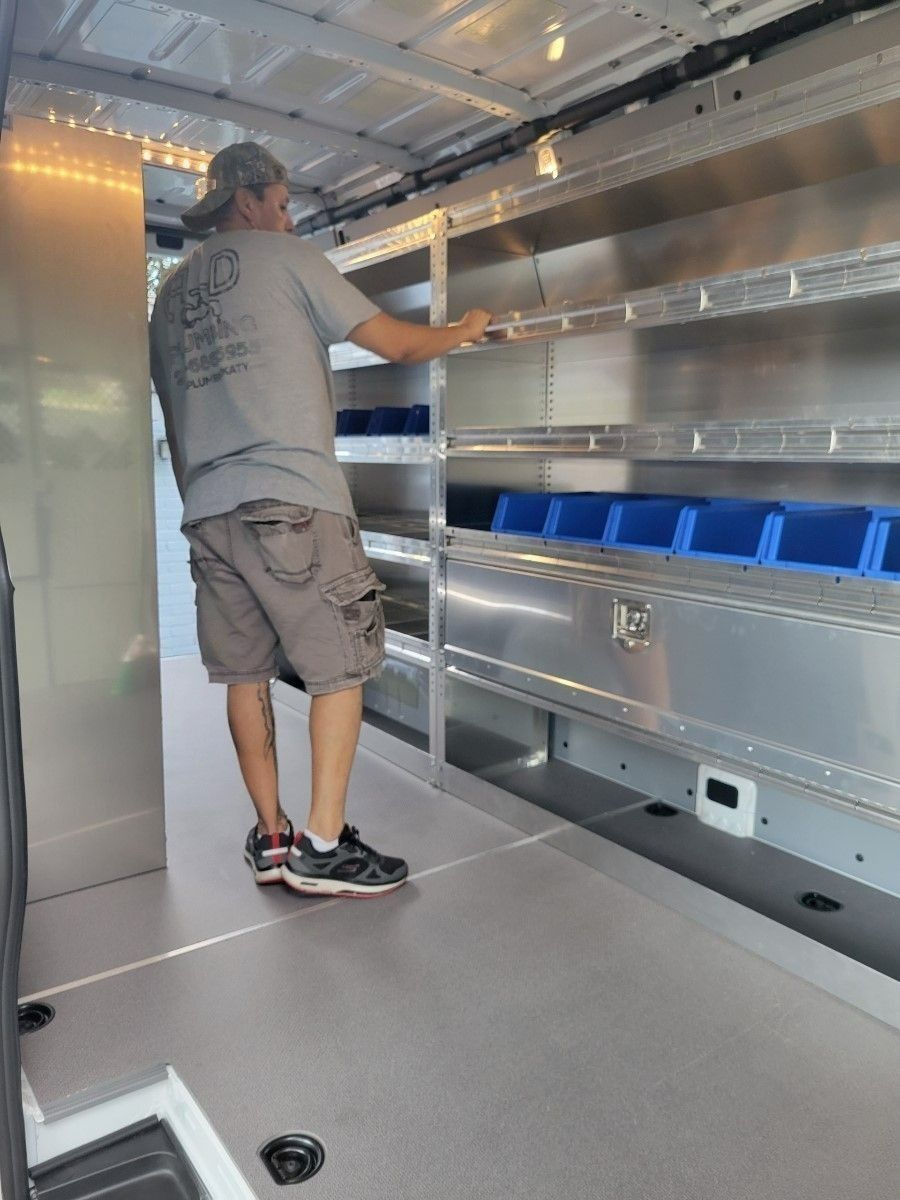 Person standing inside a cargo van, reaching toward metal shelving and blue storage bins.