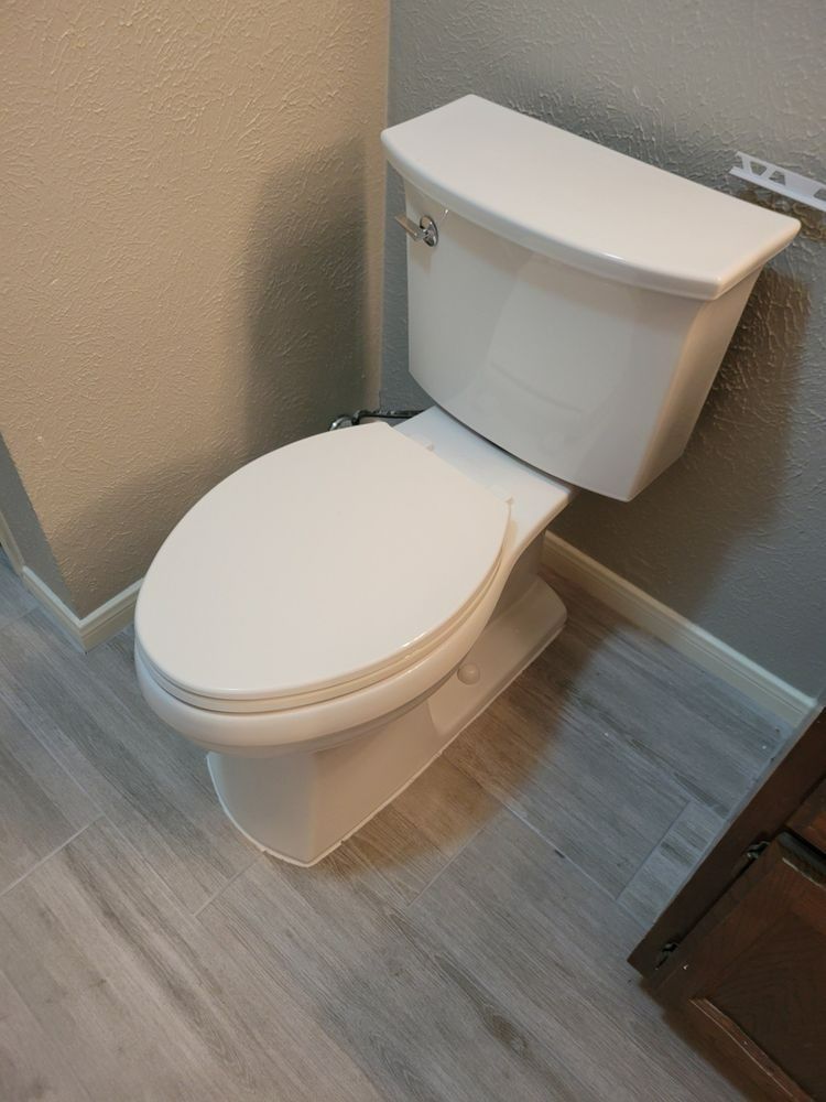 White toilet with tank in a small bathroom corner with wood-look flooring and beige walls