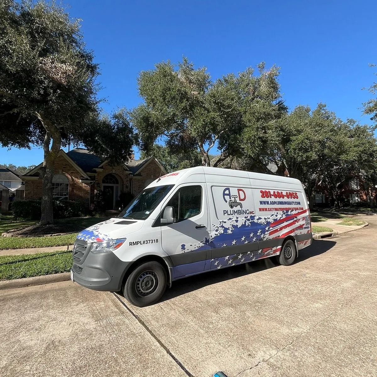 White delivery van with red and blue graphics parked on a sunny street by trees and houses.