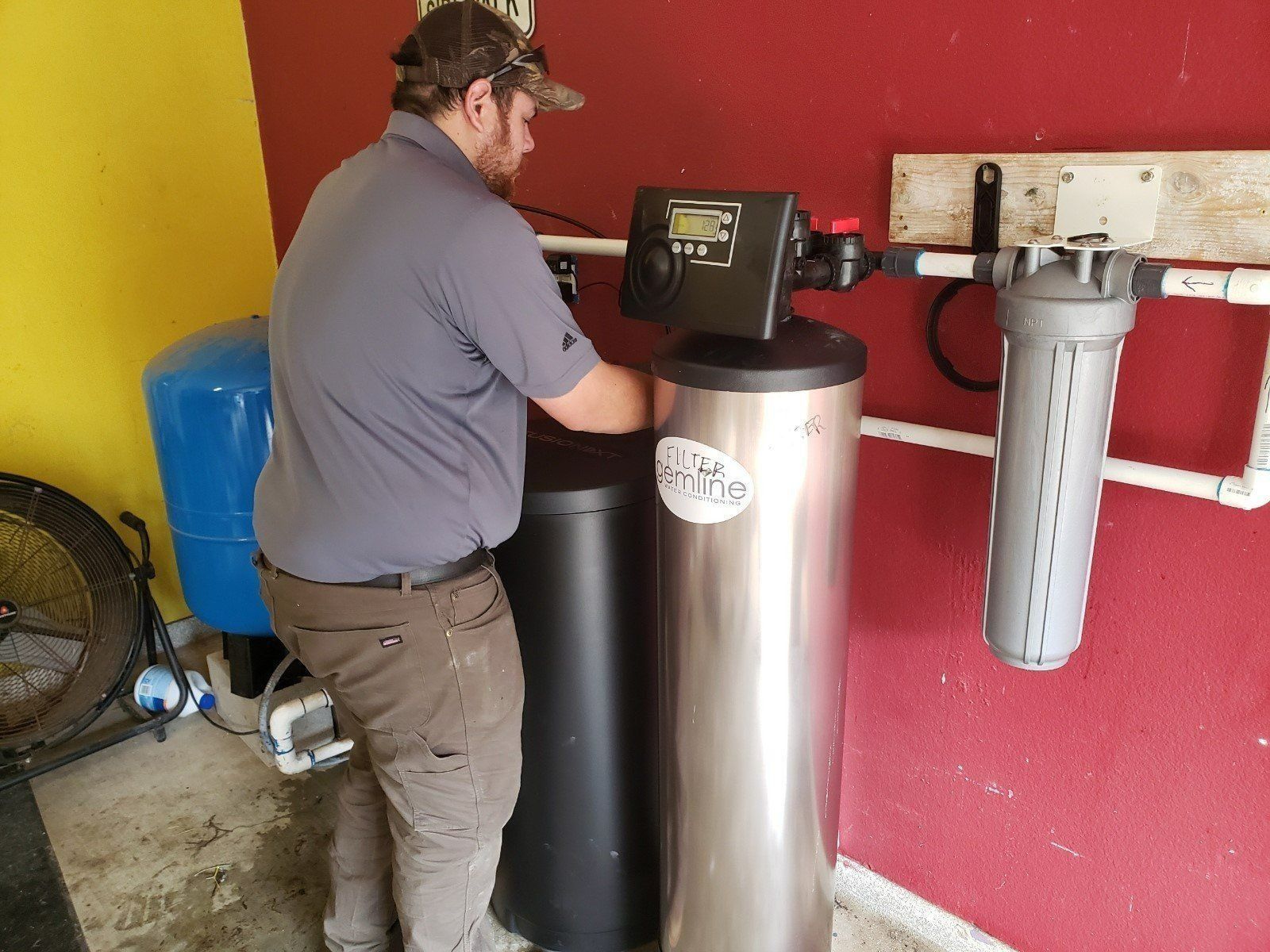 Technician servicing a water softener system beside large filter tanks in a utility room