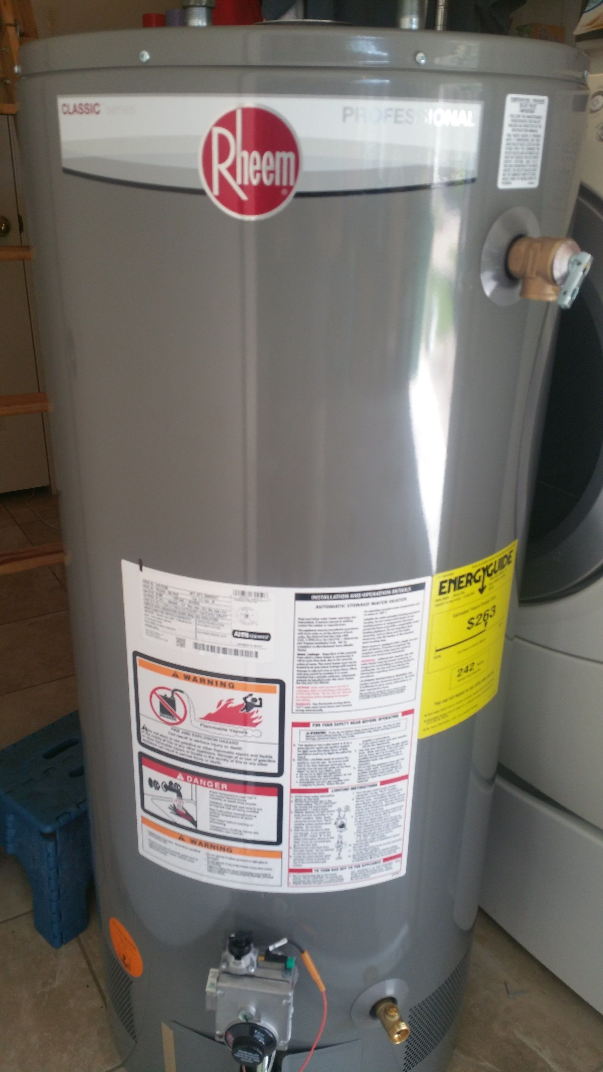 Gray Rheem water heater with labels and pipes in a utility room
