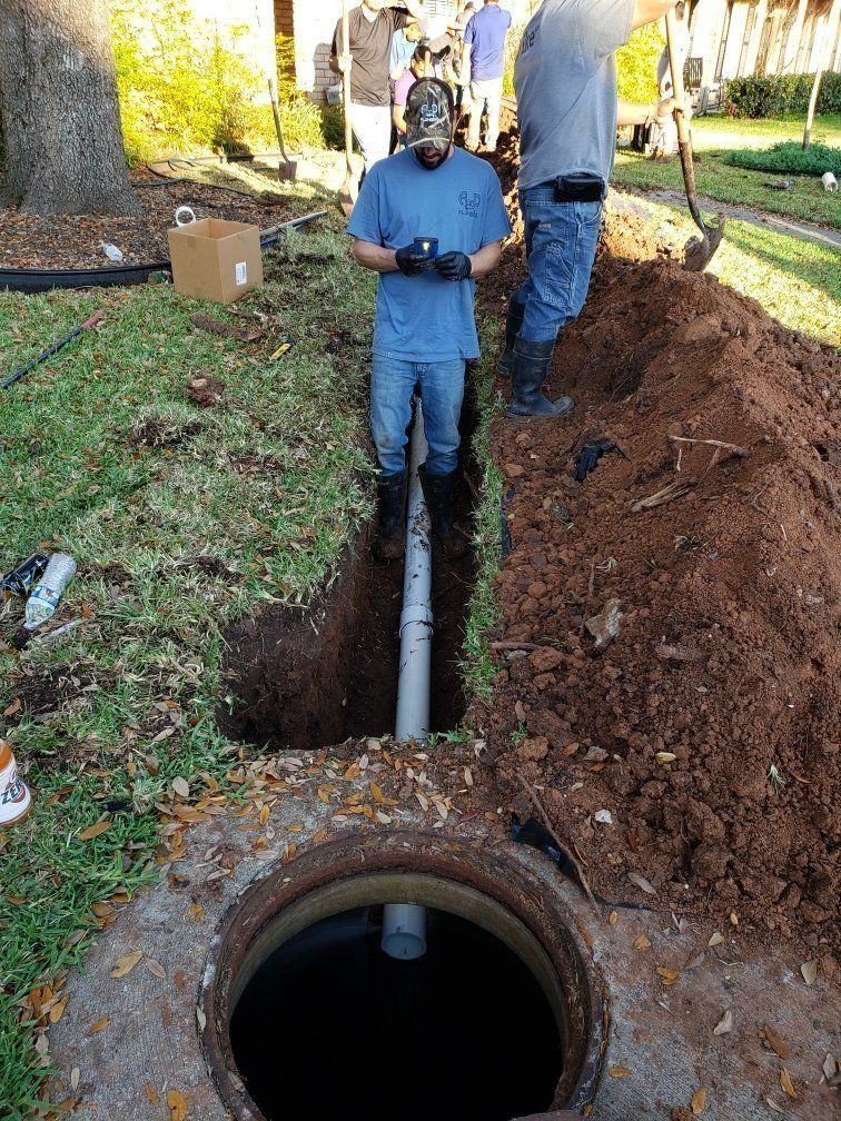 Worker standing by an open trench beside a large pipe and utility hole in a grassy yard