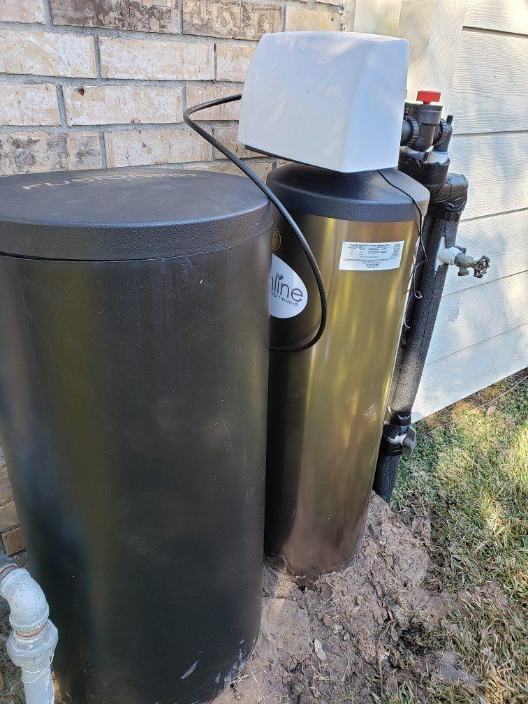 Outdoor water softener and tank beside a brick house wall, with pipes and grass nearby