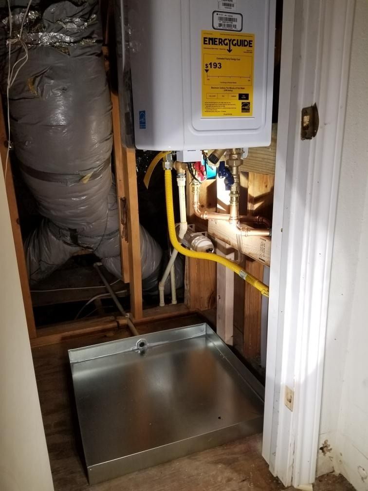 Open attic access hatch beneath a water heater, with ductwork and pipes in a utility closet.